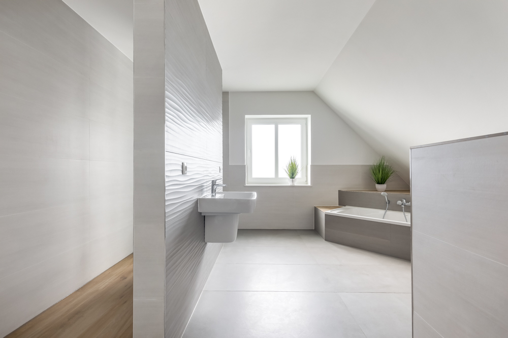 Modernes, helles Badezimmer mit Badewanne, Waschbecken und zwei Pflanzen am Fenster.