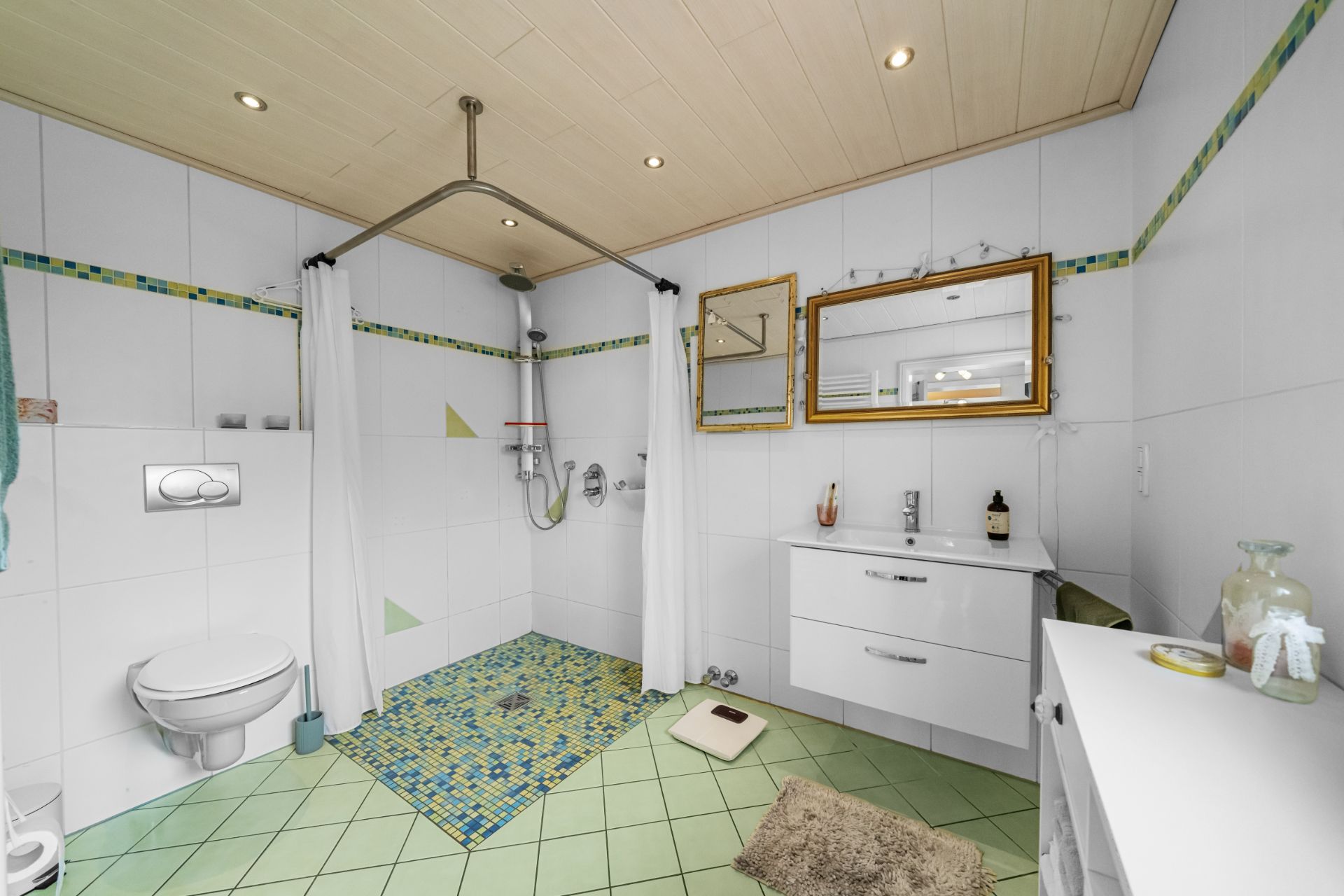 Helles Badezimmer mit begehbarer Dusche, Vorhang, Waschbecken, Spiegel und Toilette.
