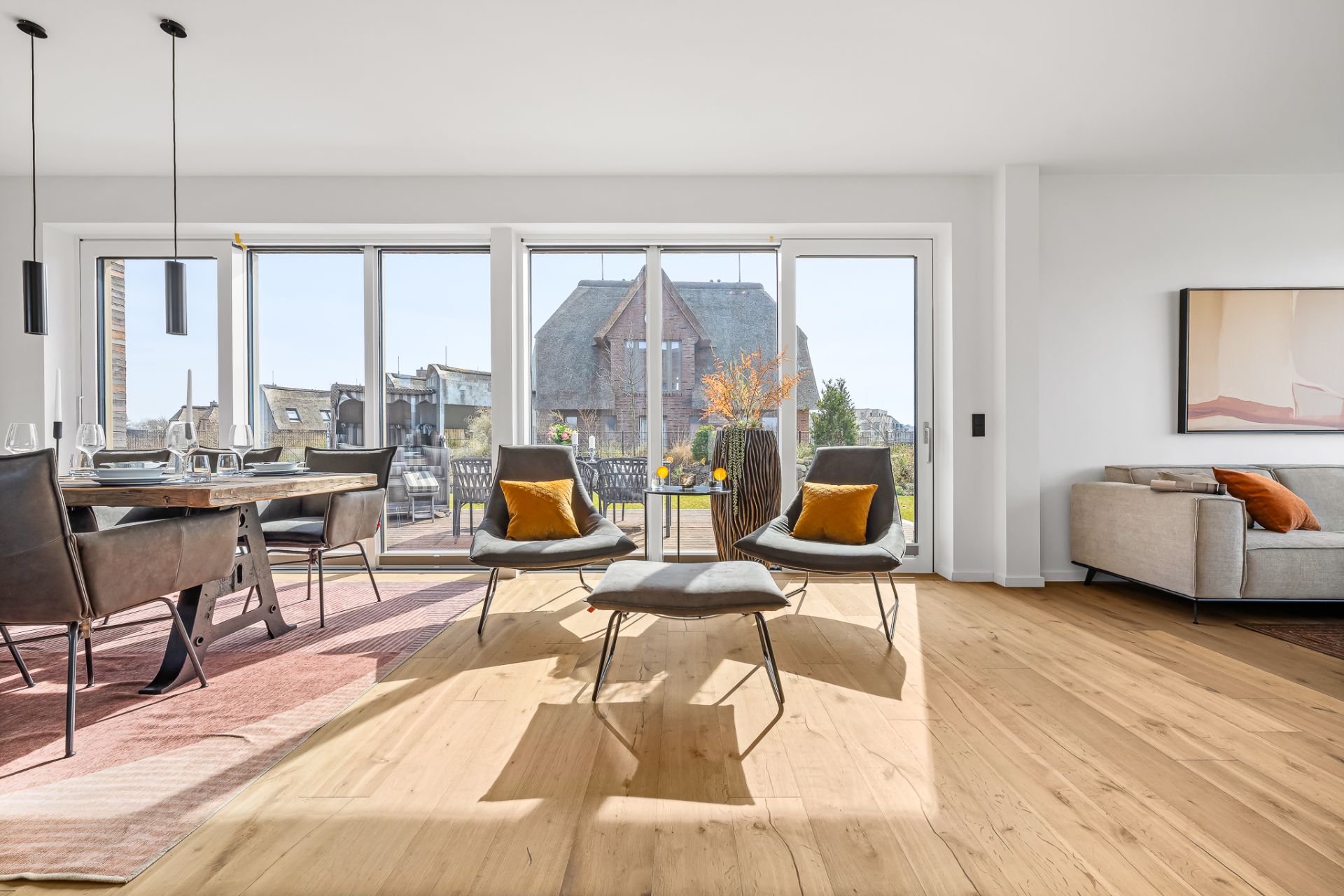 Helles Wohnzimmer mit großen Fenstern, Sitzgruppe und Esstisch auf einem Holzfußboden.