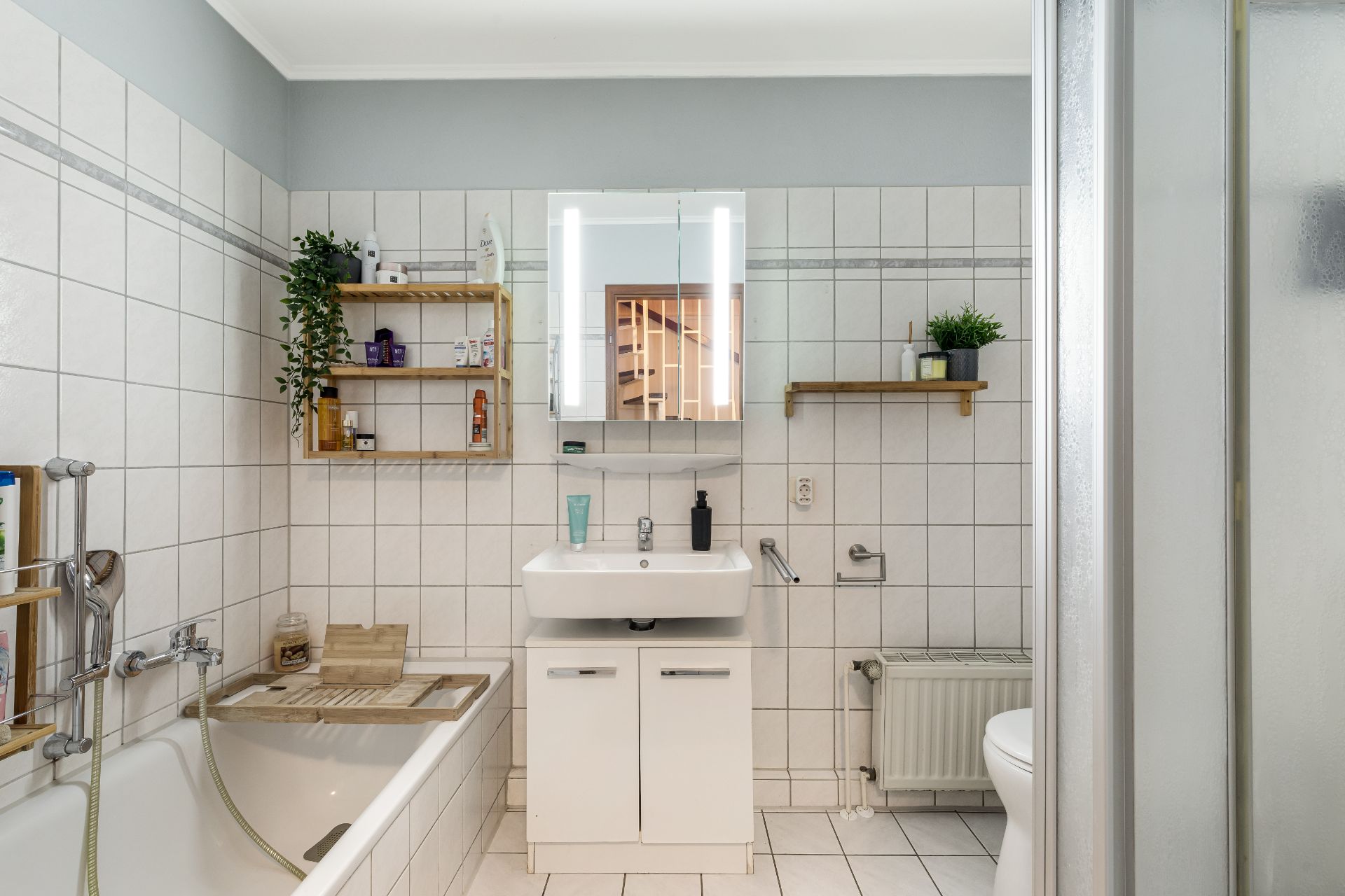 Modernes Badezimmer mit Badewanne, Waschbecken, Spiegel, Regalen und Duschkabine.