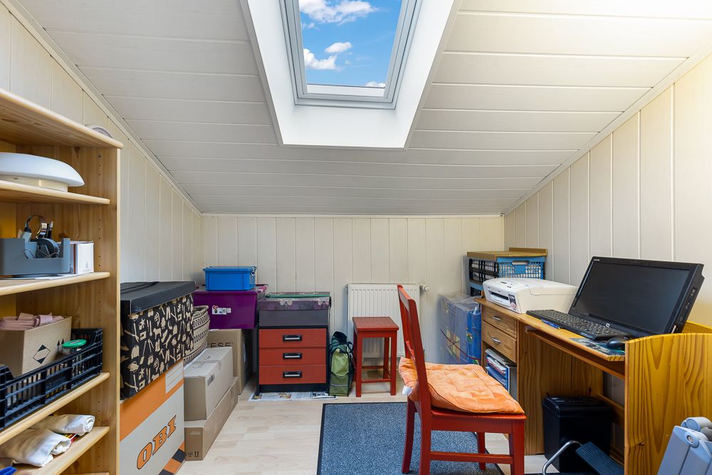 Kleines Arbeitszimmer mit Schreibtisch, Regalen und Dachfenster unter einer schrägen Decke.