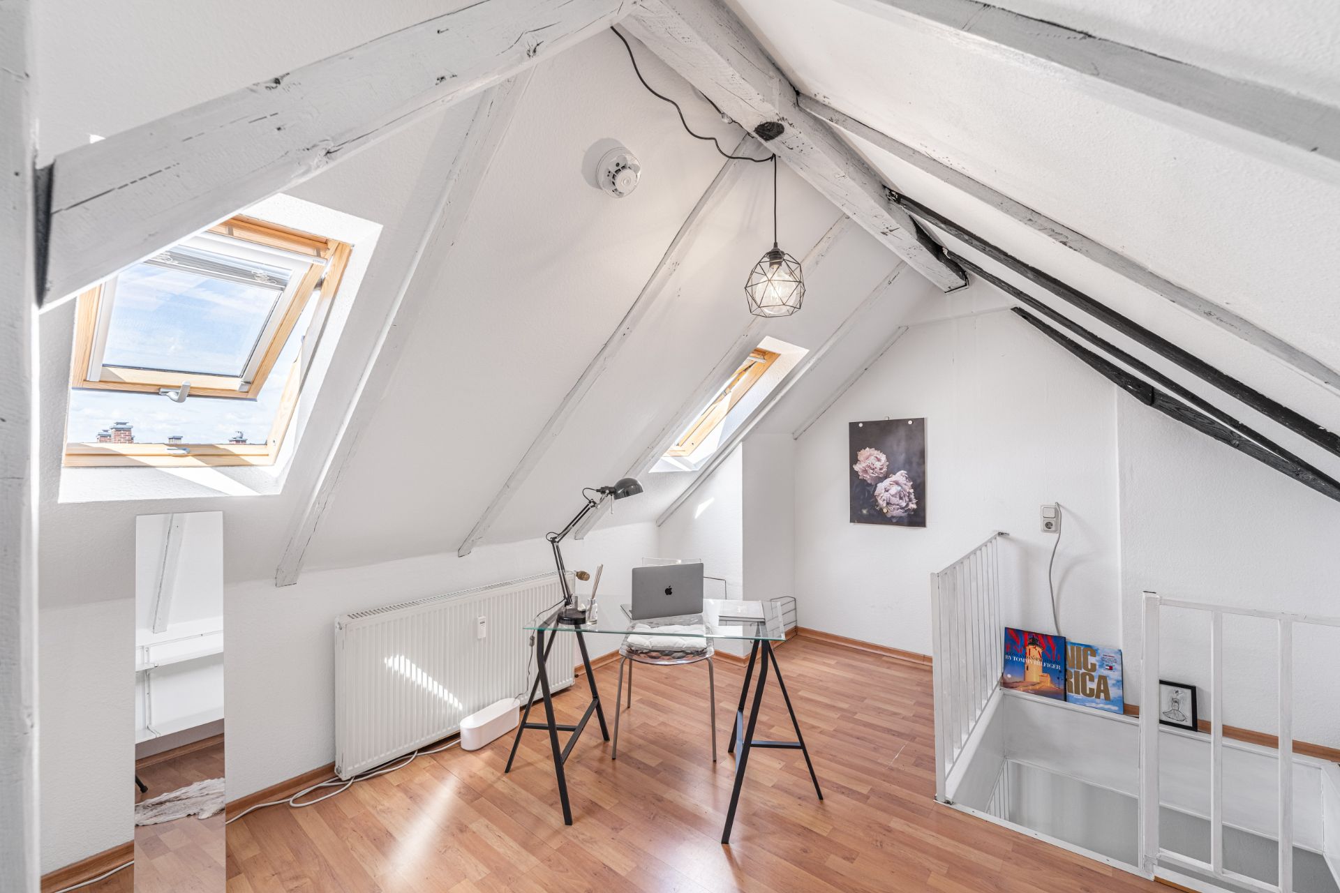 Helles Dachzimmer mit Schreibtisch, Stuhl, Dachfenstern und Holzfußboden.