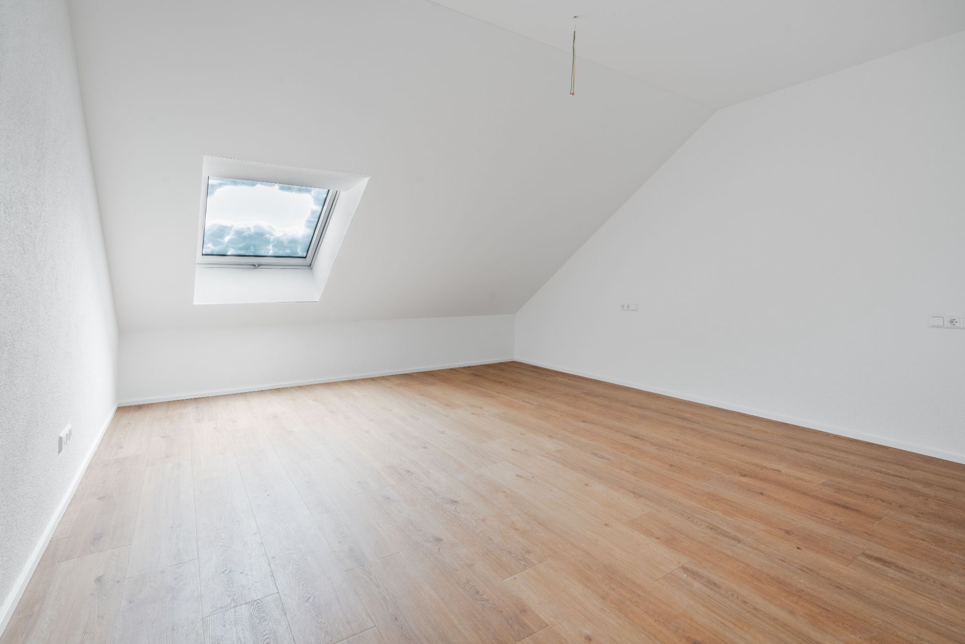 Leerer Raum mit Dachschräge, Holzfußboden und Fenster in der Schräge.