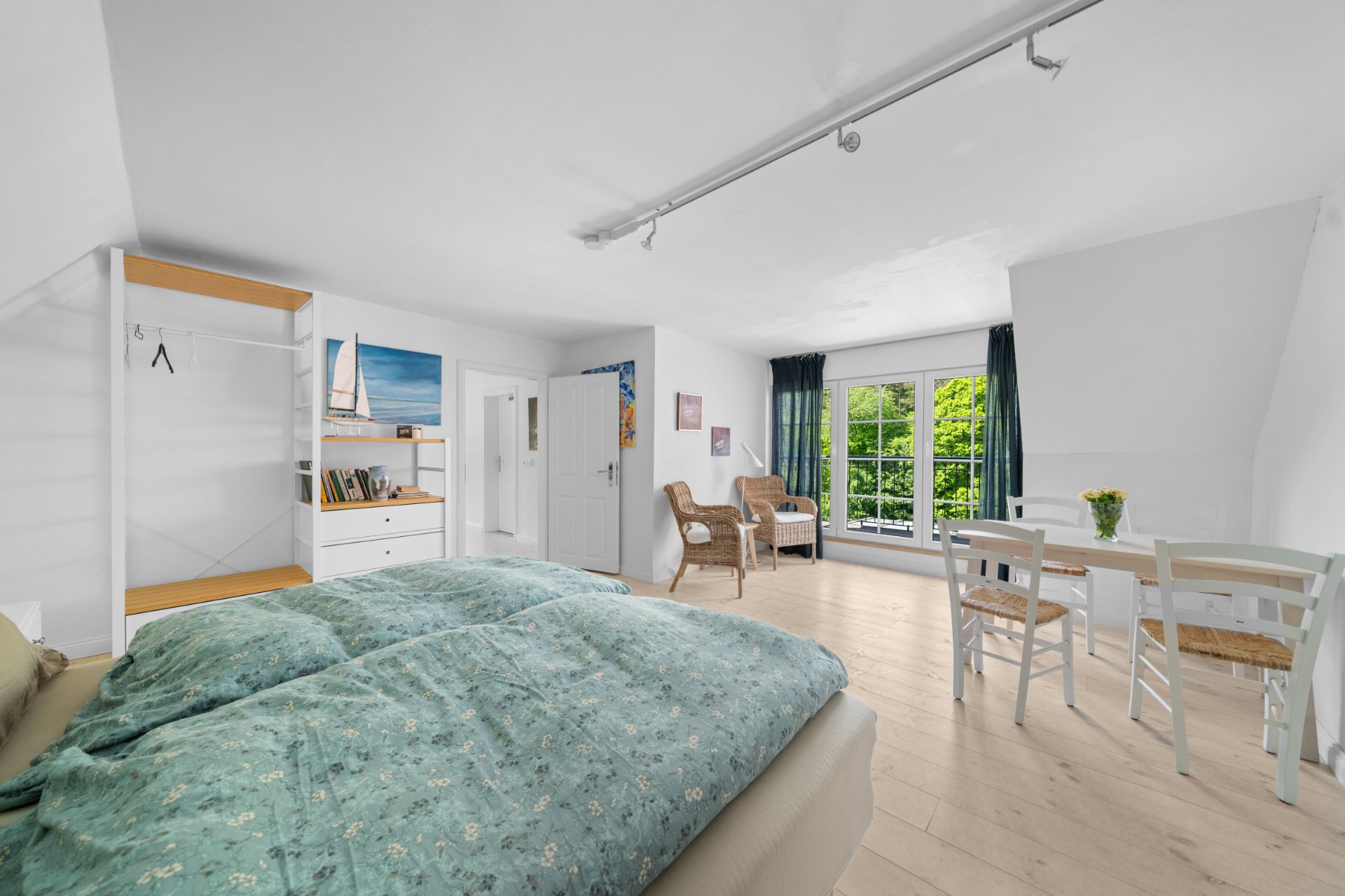 Helles Schlafzimmer mit Doppelbett, Sitzgruppe, Esstisch und großem Fenster mit Blick ins Grüne.