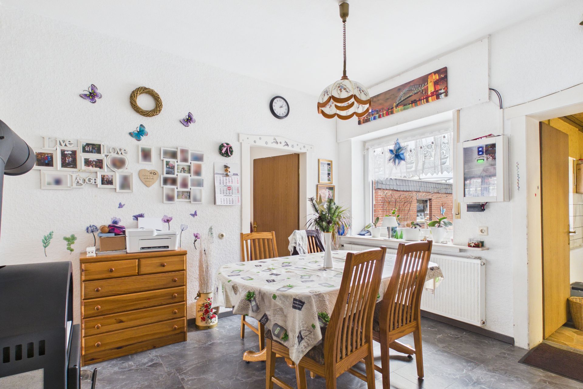 Esszimmer mit Holztisch, vier Stühlen, Kommode und Wanddeko, großes Fenster mit Blick nach draußen.