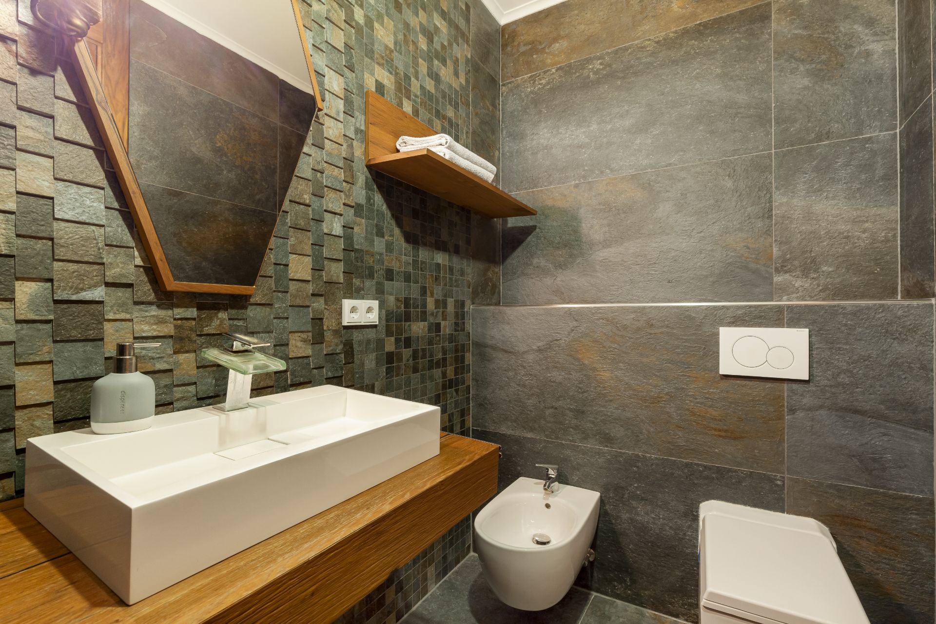 Modernes Badezimmer mit Waschbecken, Bidet, WC und Wandregal mit Handtüchern.