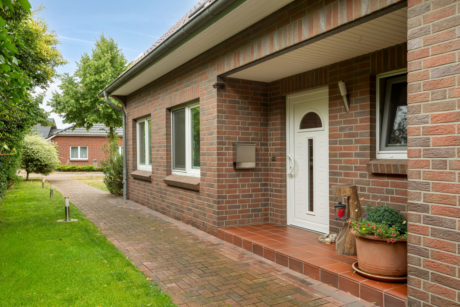 Backsteinhaus mit weißer Haustür, zwei Fenstern und bepflanztem Blumentopf am Eingang.