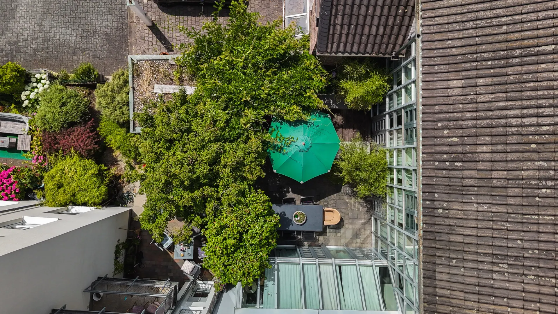 Innenhof mit Bäumen, Sitzbereich und grünem Sonnenschirm, von oben gesehen.