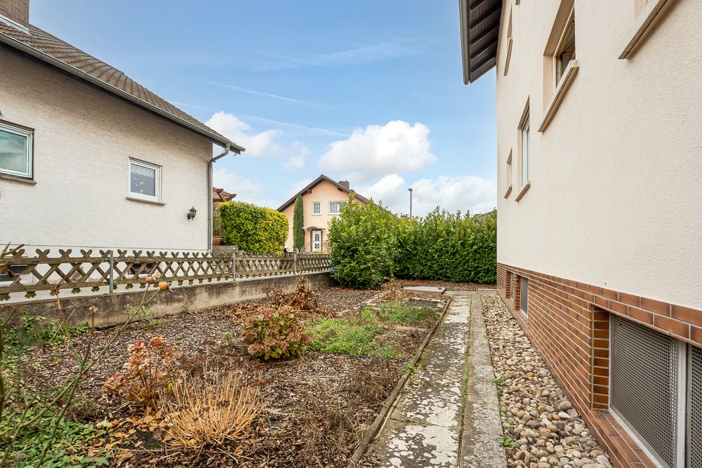 Gartenbereich mit Gehweg neben einem Wohnhaus, Sicht auf Nachbarhäuser und Hecke.