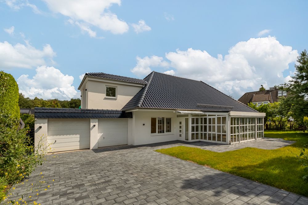 Modernes Einfamilienhaus mit großem Wintergarten, zwei Garagen und gepflasterter Einfahrt.
