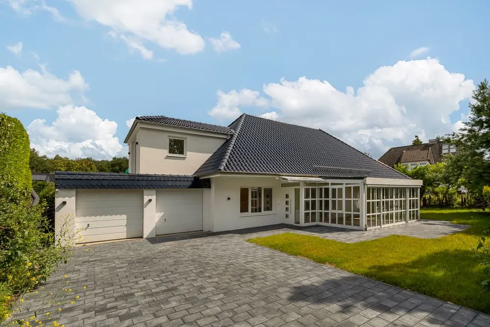 Modernes Einfamilienhaus mit großem Wintergarten, zwei Garagen und gepflasterter Einfahrt.