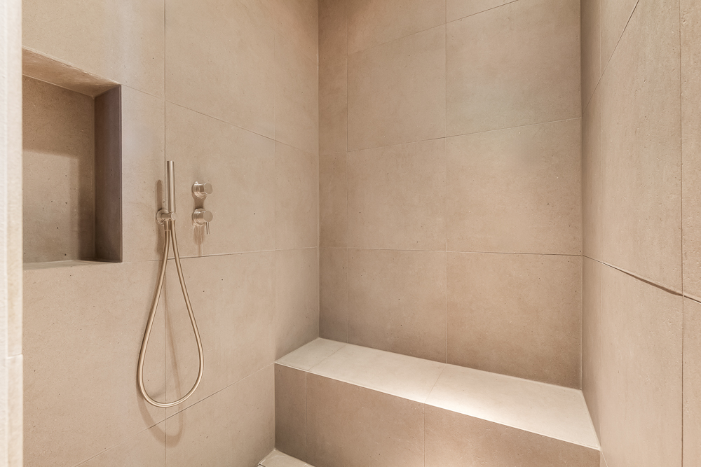 Moderne, begehbare Dusche mit Bank und Nische in beige gefliesten Wänden.