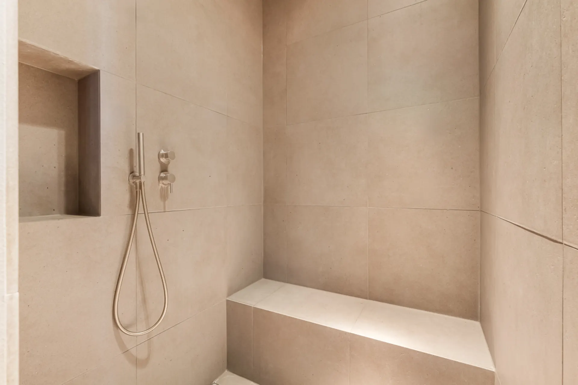 Moderne, begehbare Dusche mit Bank und Nische in beige gefliesten Wänden.