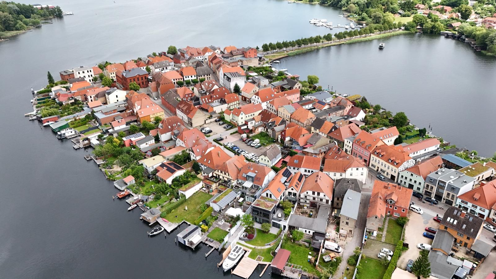 Luftaufnahme einer kleinen Stadt mit roten Dächern an einem Seeufer.