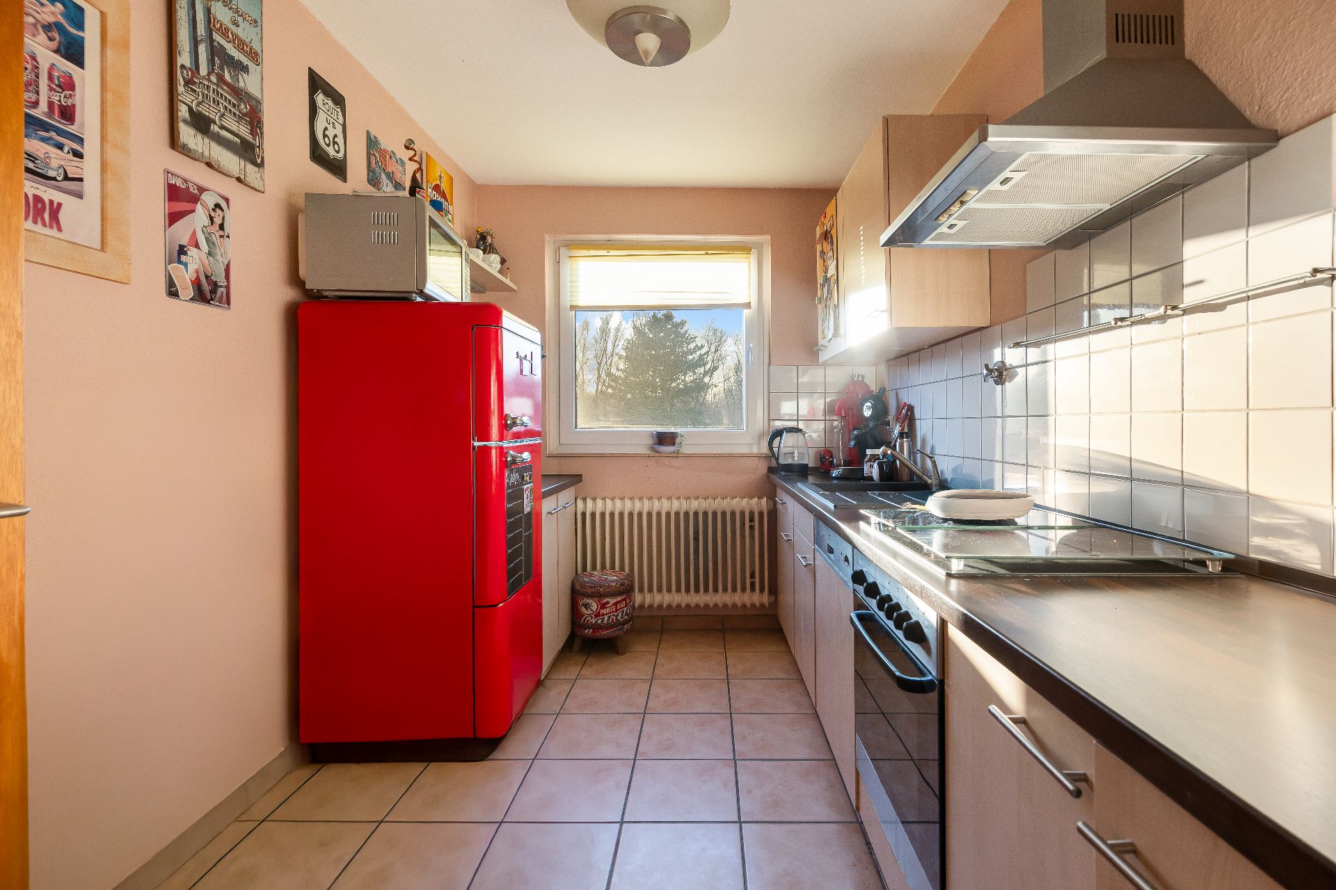 Küche mit rotem Kühlschrank, Herd, Spüle und Fenster im Hintergrund.