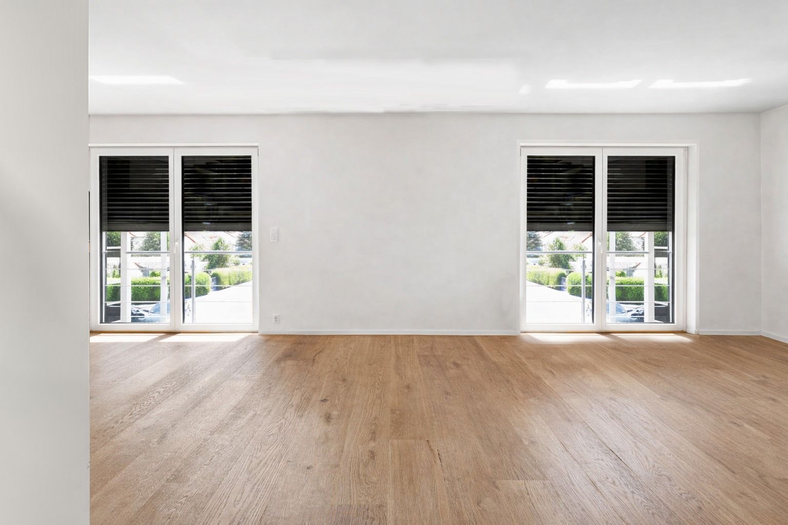 Leerer Raum mit Holzfußboden und zwei Fenstertüren mit halb geschlossenen Rollläden.