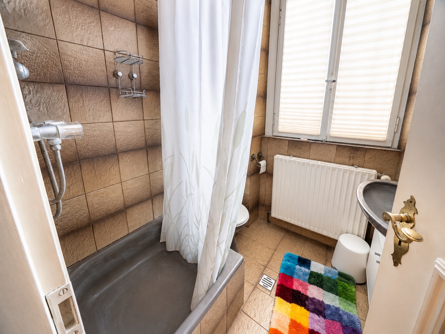 Kleines Badezimmer mit Badewanne, Duschvorhang, Waschbecken, Toilette und buntem Teppich.