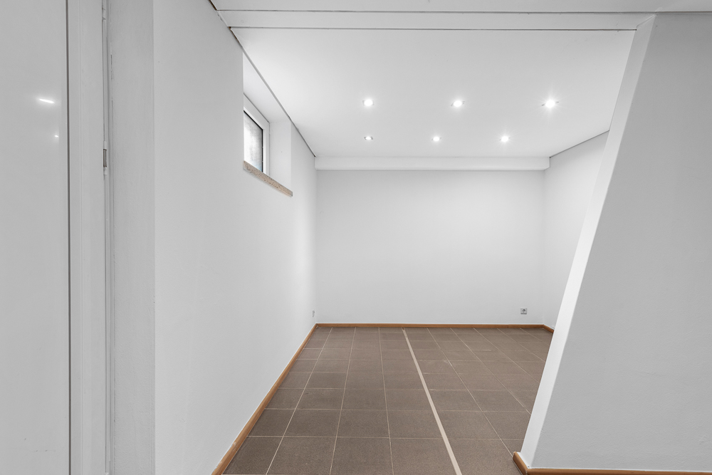 Leerer, weiß gestrichener Raum mit Fliesenboden und kleinem Fenster an der Wand.