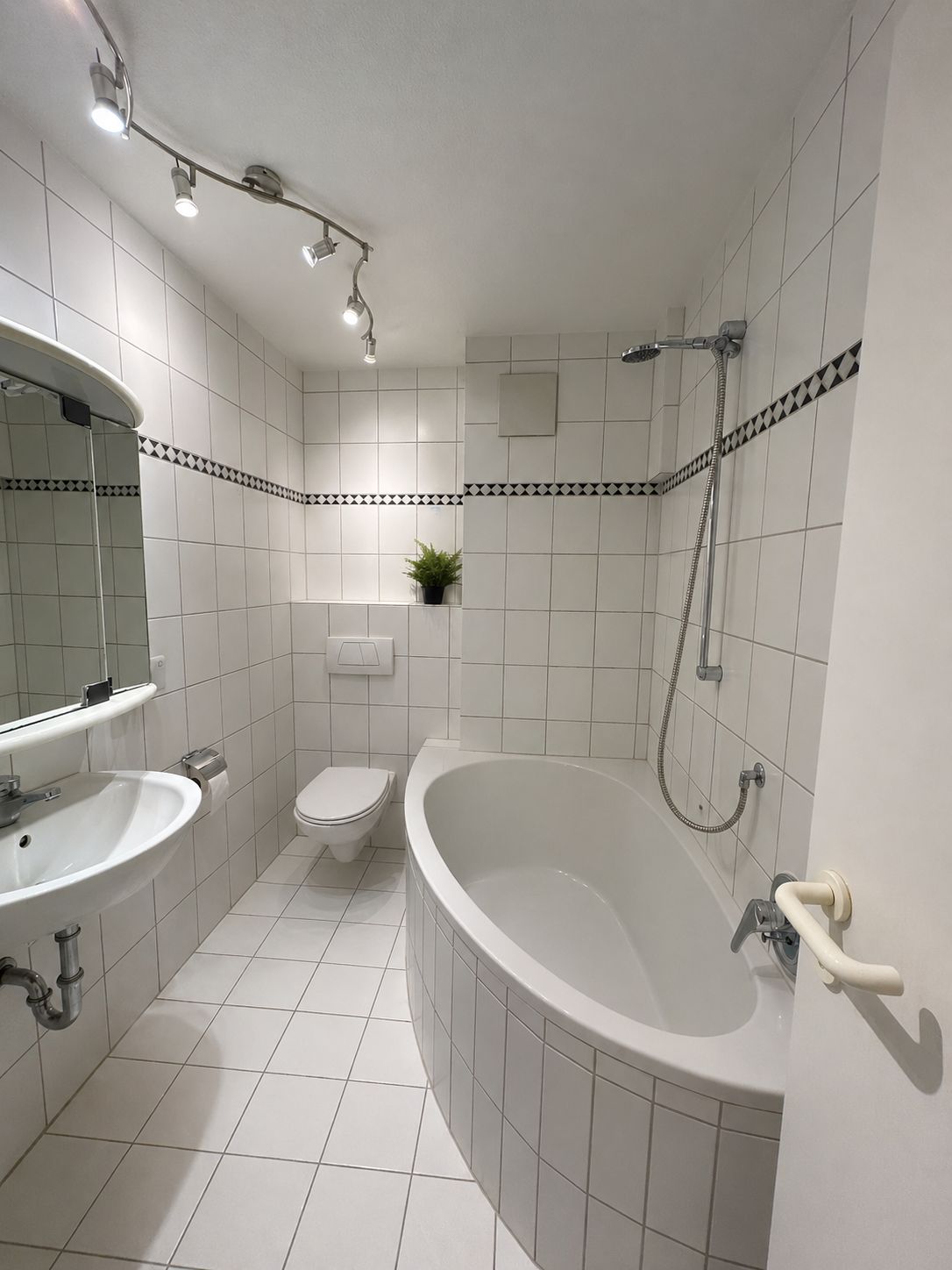 Modernes Bad mit weißer Badewanne, Waschbecken, Toilette und Wandspiegel, alles gefliest.