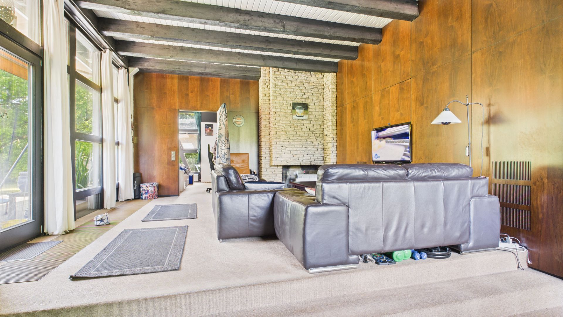 Wohnzimmer mit braunen Wänden, großen Fenstern, Kamin und zwei dunklen Ledersofas.