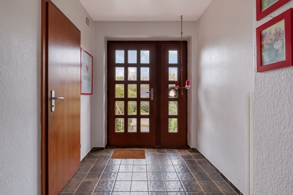 Flur mit brauner Eingangstür, einer Holztür links und Fliesenboden.