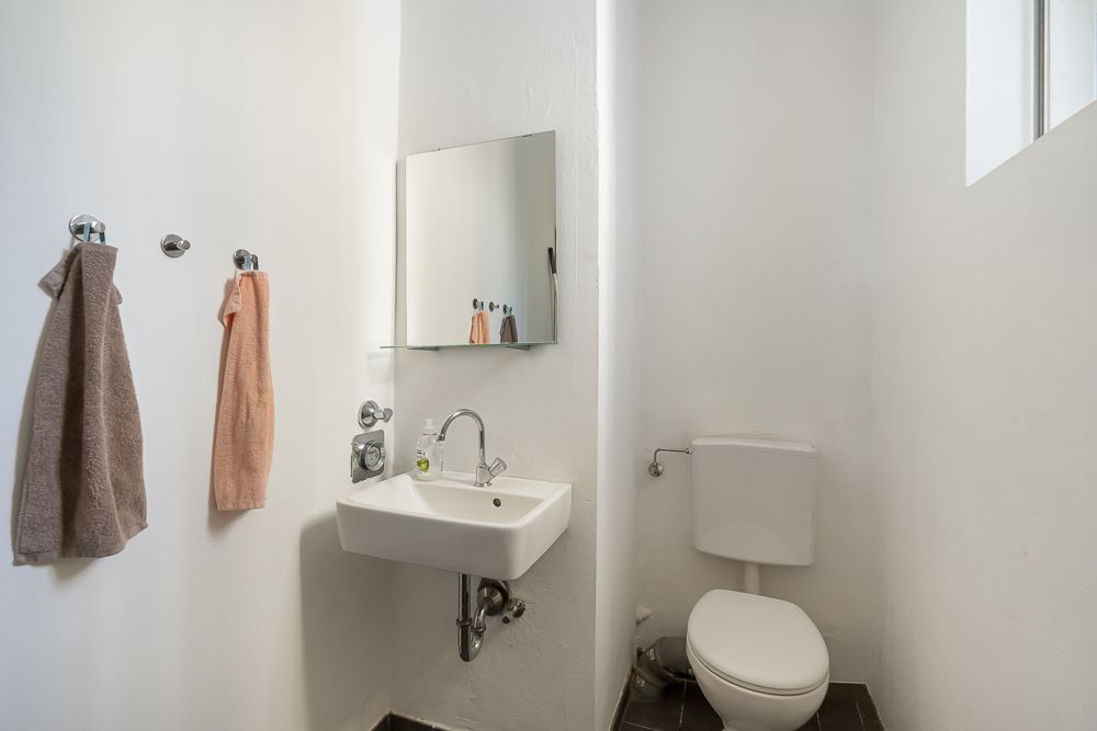 Kleines Badezimmer mit Waschbecken, Spiegel, Toilette und zwei Handtüchern an der Wand.