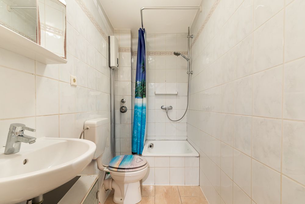 Kleines Badezimmer mit Waschbecken, Toilette, Badewanne und Duschvorhang mit Naturmotiv.