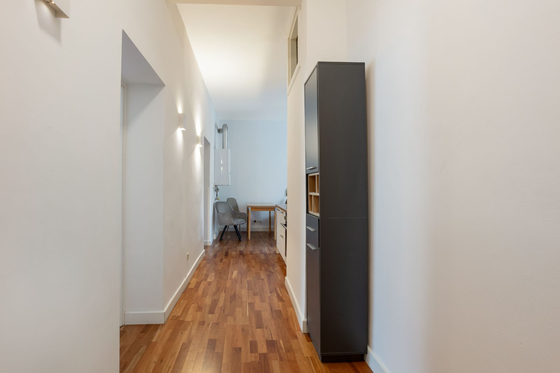 Langer Flur mit Holzfußboden, seitlicher Schrank und Blick auf Tisch und Stuhl am Ende.