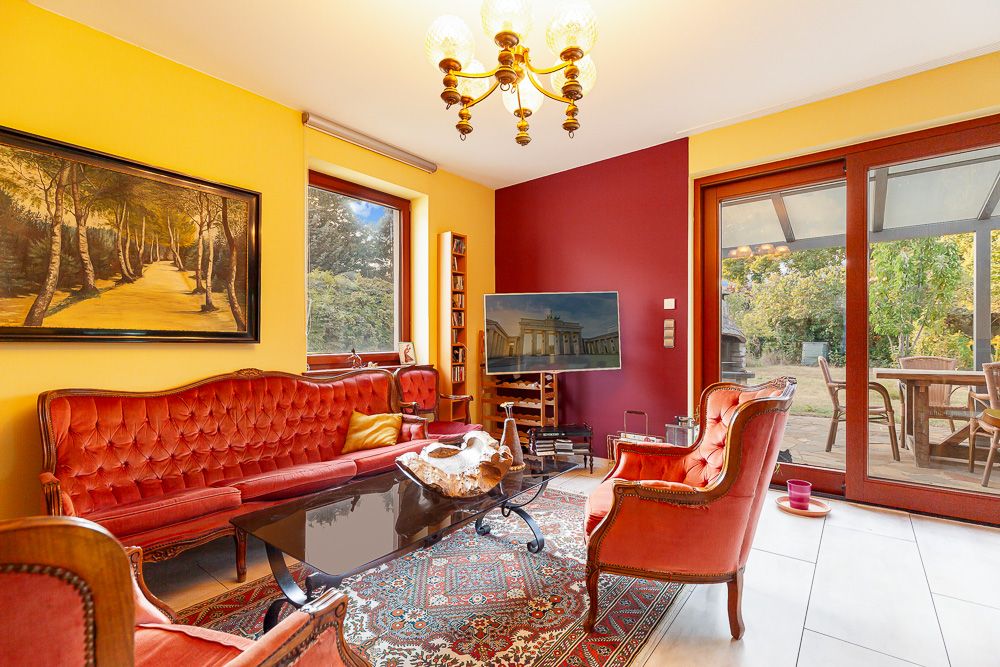 Wohnzimmer mit roten Polstermöbeln, Teppich, Fernseher und Zugang zur Terrasse mit Gartenblick.