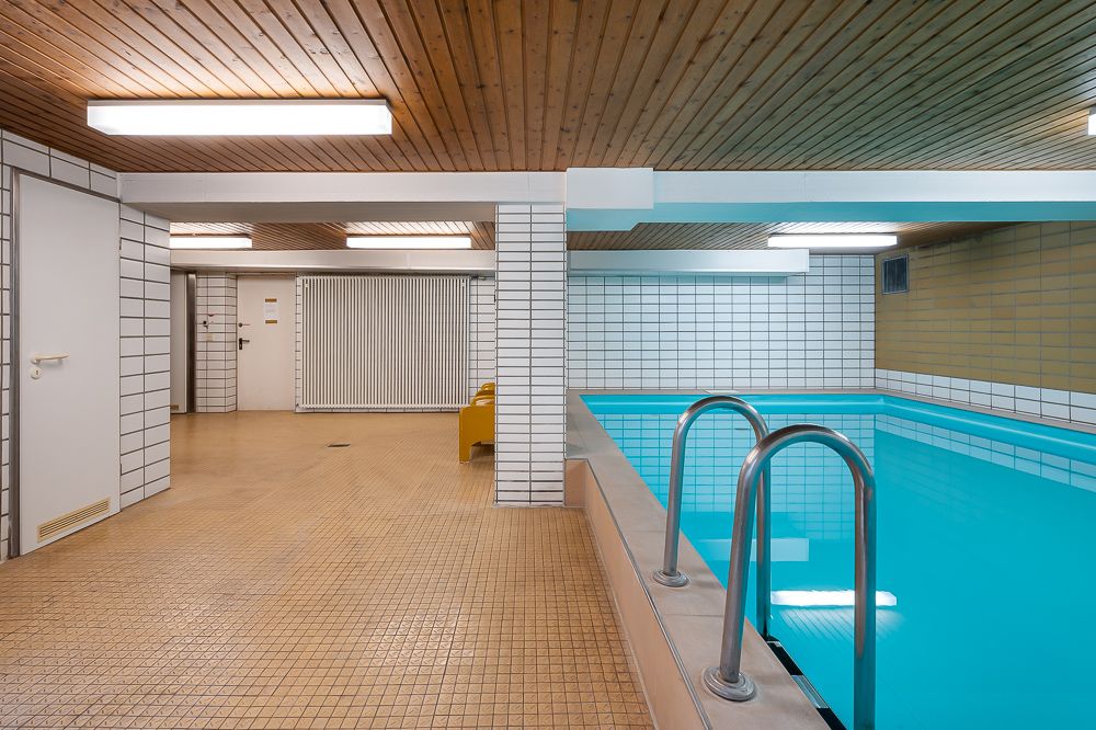 Innenpool mit Fliesenwänden, gelber Bank und Holzdecke in einem Wohngebäude.