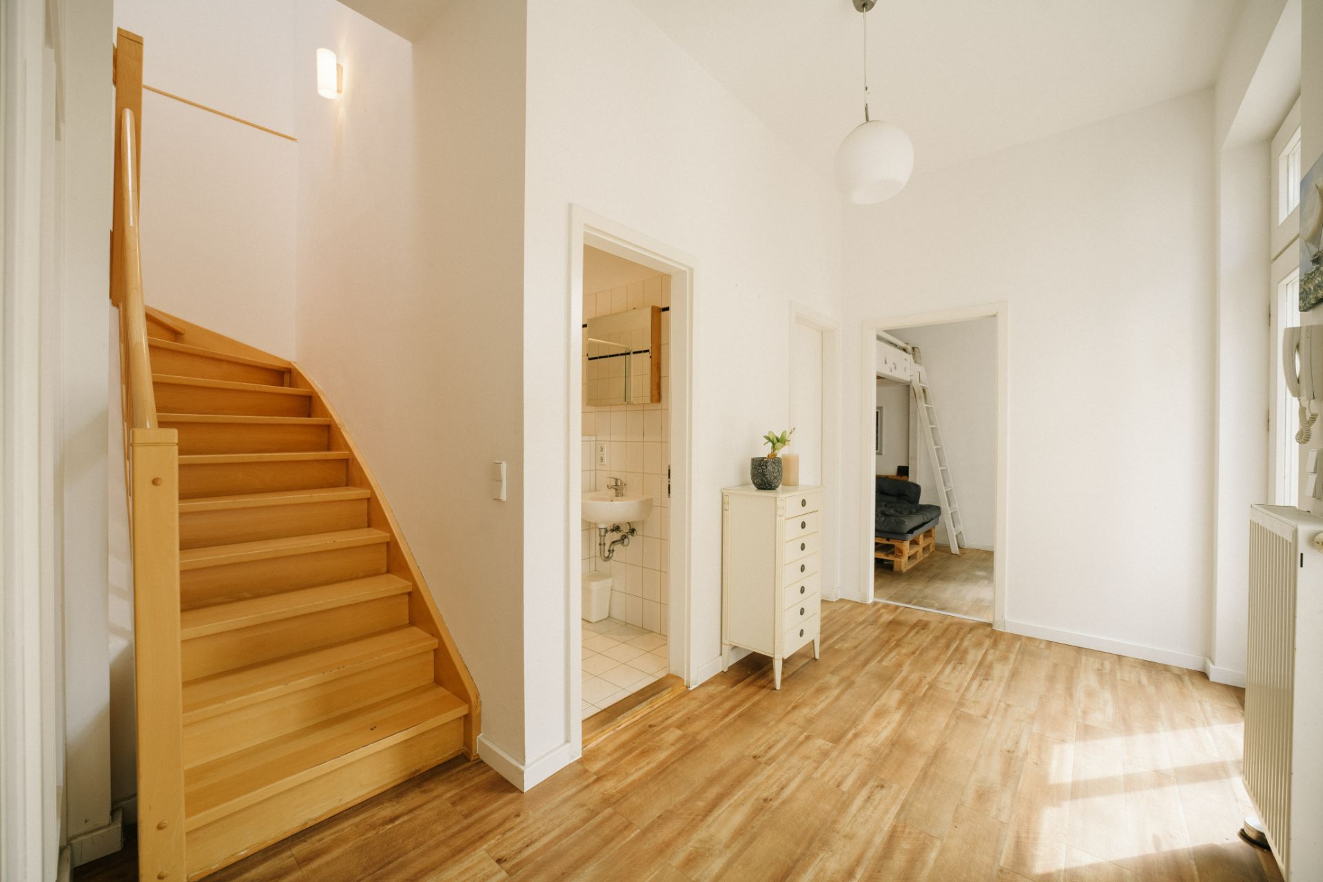 Heller Flur mit Holztreppe, Kommode, Zugang zu Bad und Zimmer mit Hochbett.