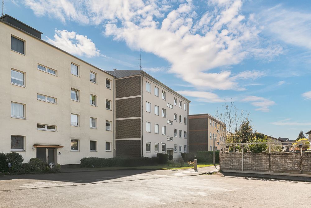 Mehrstöckiges Wohngebäude mit vielen Fenstern und einem gepflasterten Vorplatz.