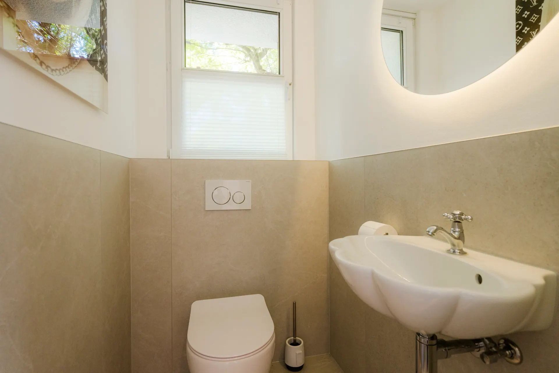 Modernes Gäste-WC mit Waschbecken, Toilette und Fenster, helle Fliesen an den Wänden.