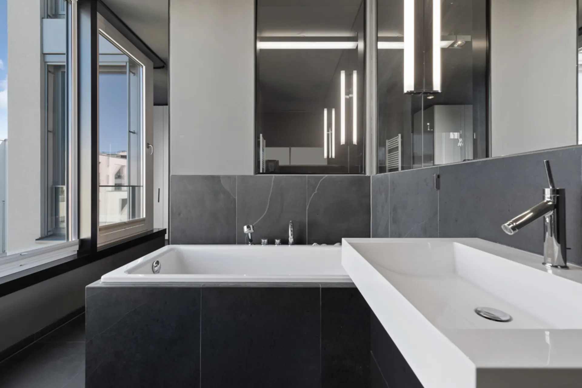 Modernes Badezimmer mit großer Badewanne, Waschbecken und offenem Fenster.