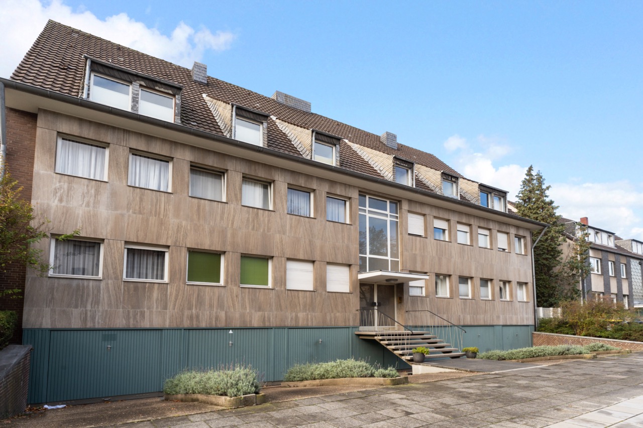 Mehrfamilienhaus mit mehreren Fenstern, Eingangsbereich mit Treppe und Pflanzen davor.