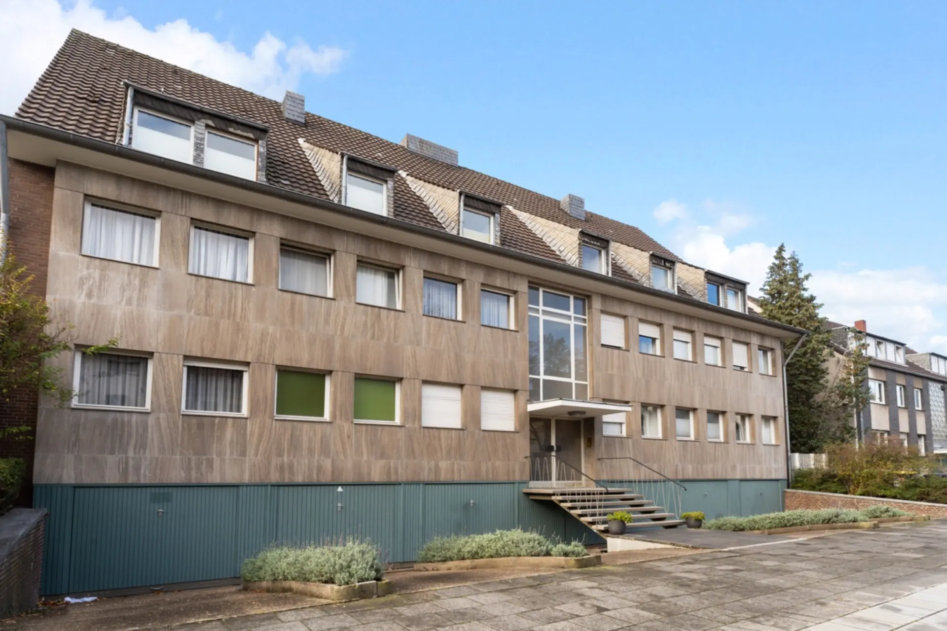 Mehrfamilienhaus mit mehreren Fenstern, Eingangsbereich mit Treppe und Pflanzen davor.
