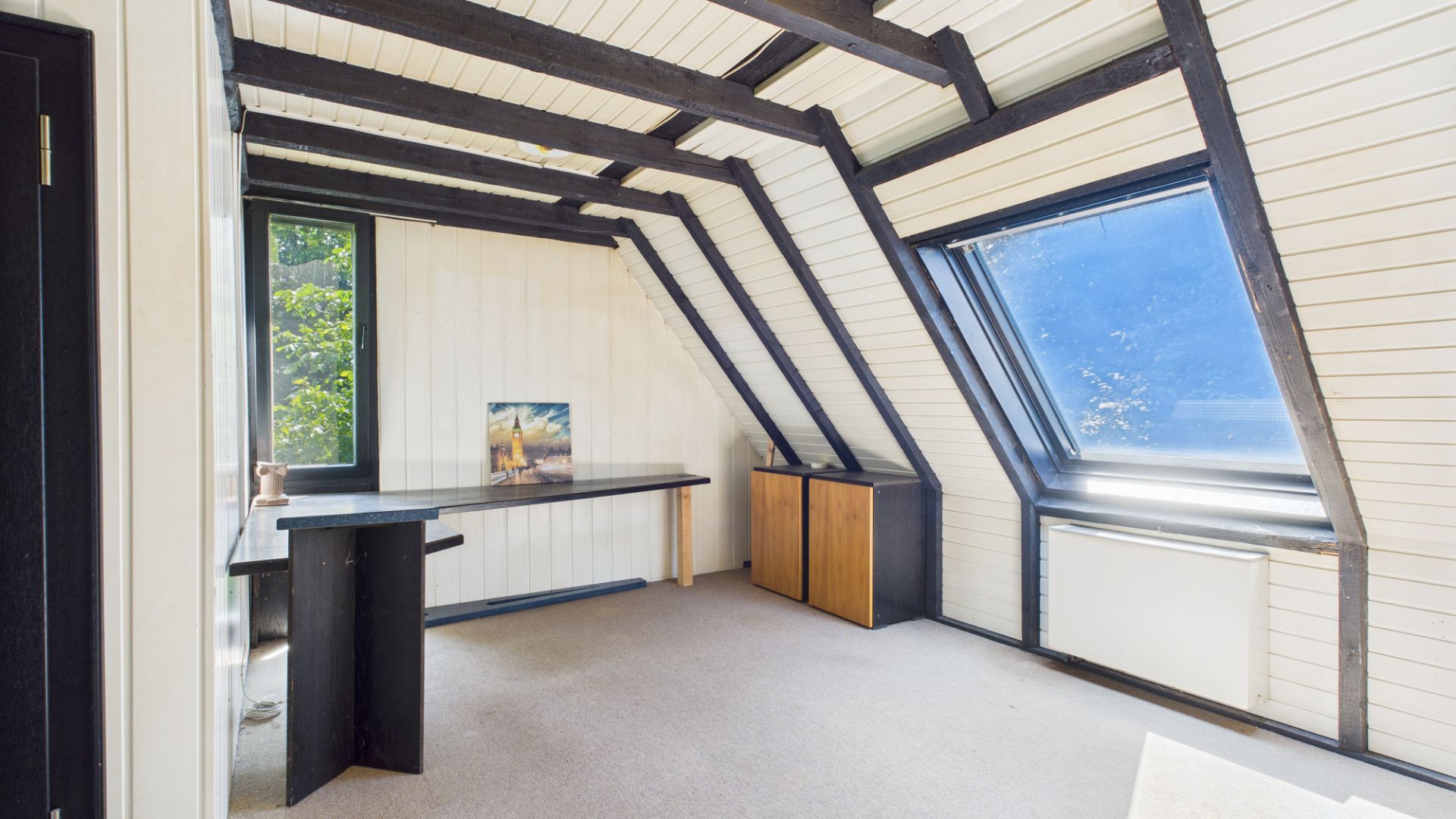 Heller Dachraum mit Schreibtisch, Fenster und sichtbaren Holzbalken.