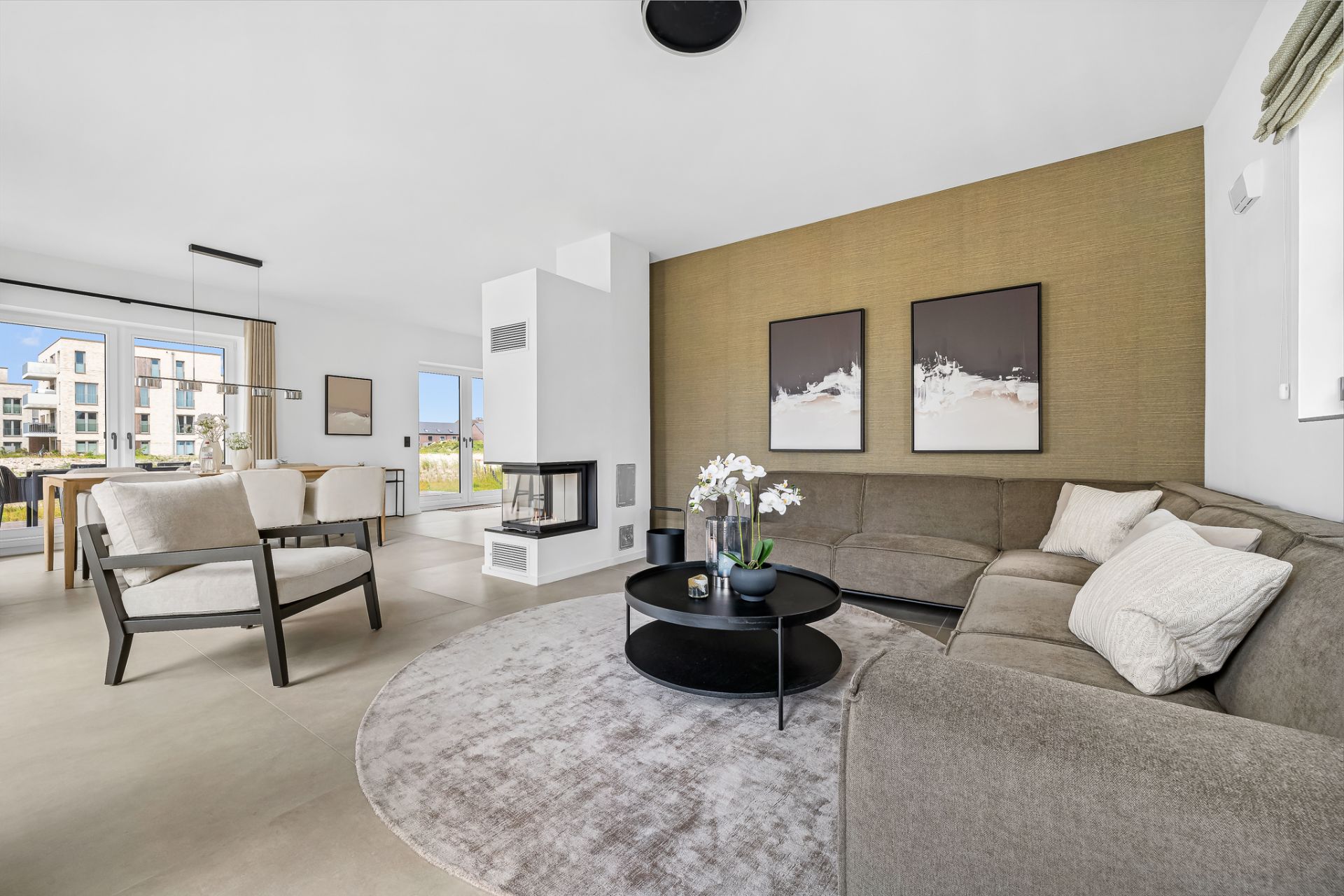 Modernes Wohnzimmer mit großer Eckcouch, rundem Teppich und Kamin, Essbereich im Hintergrund.