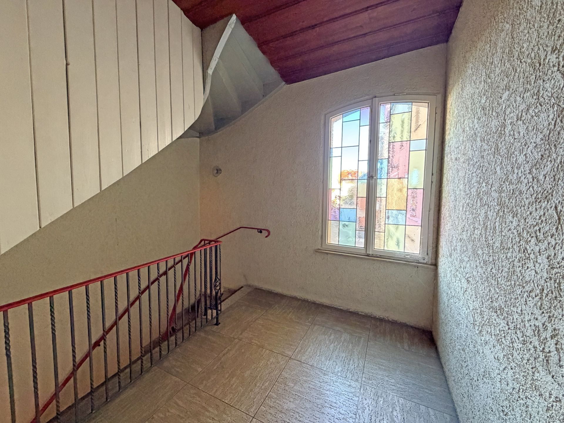 Treppenhaus mit rotem Geländer und buntem Fenster an der Wand.