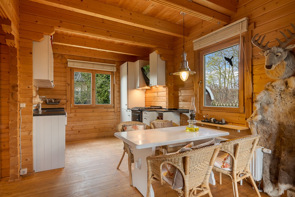 Holz-Küche mit Esstisch, Stühlen, großen Fenstern und Tierpräparat an der Wand.
