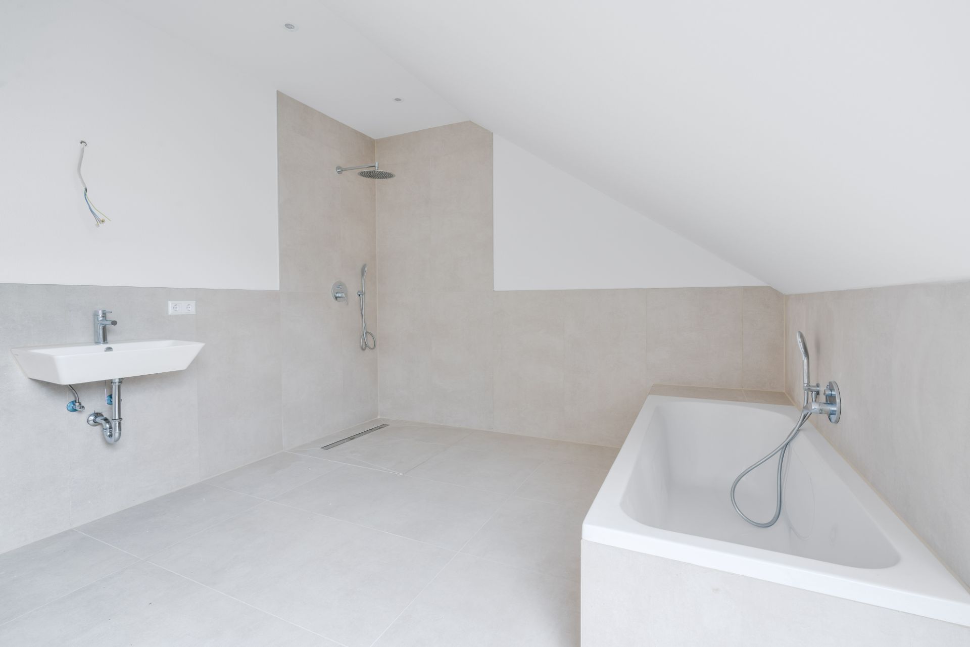 Helles Badezimmer mit Badewanne, Dusche und Waschbecken unter einer Dachschräge.