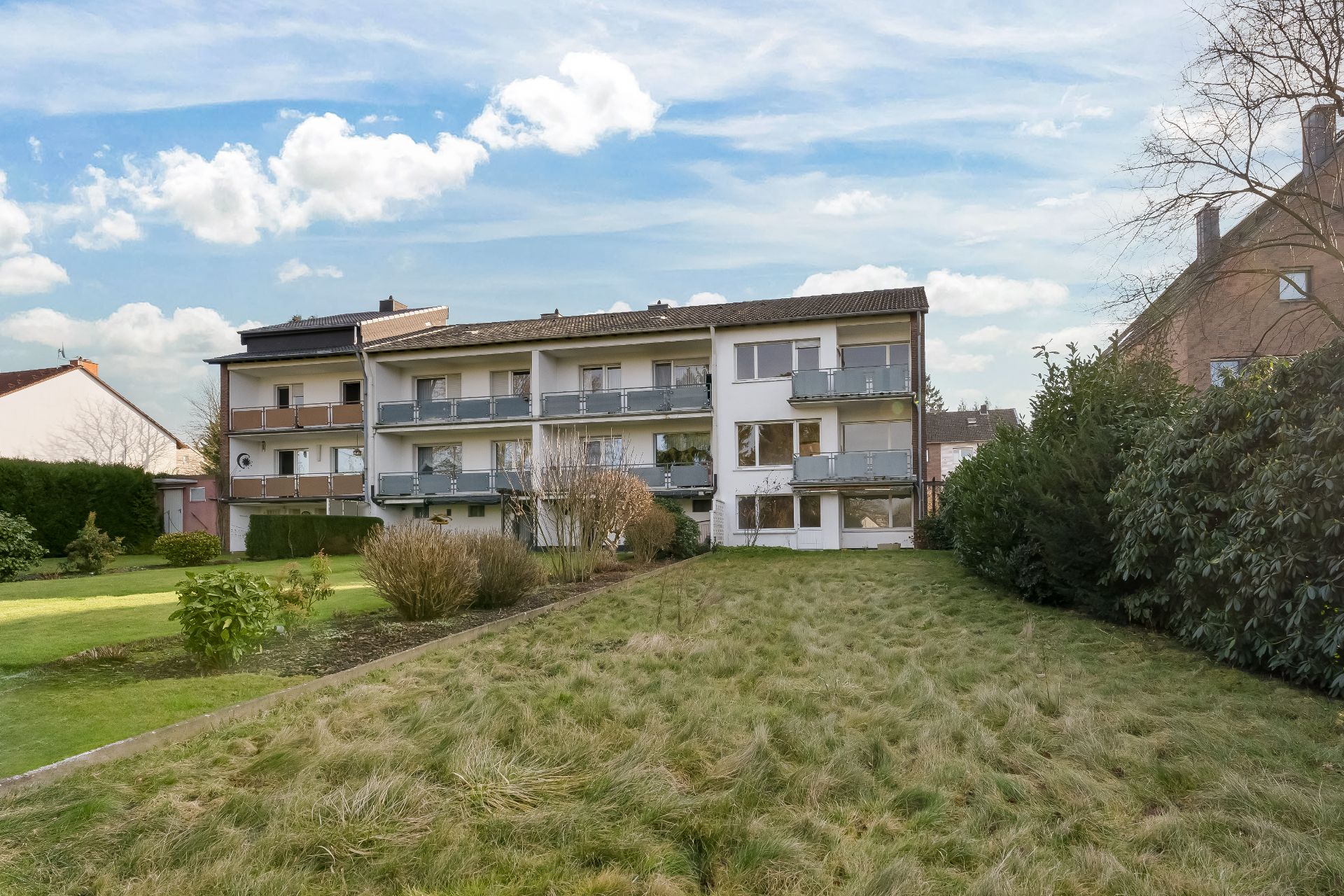 Dreistöckiges Wohngebäude mit Balkonen und großem Garten im Vordergrund.