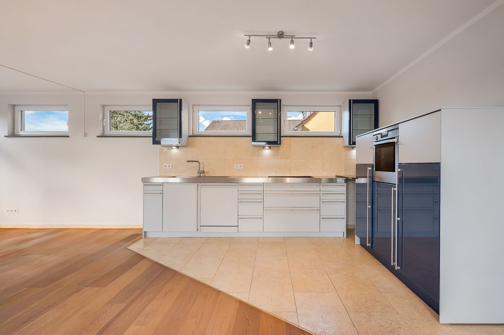 Moderne Einbauküche mit weißen Schränken, Edelstahl-Arbeitsplatte und hellen Holzböden.