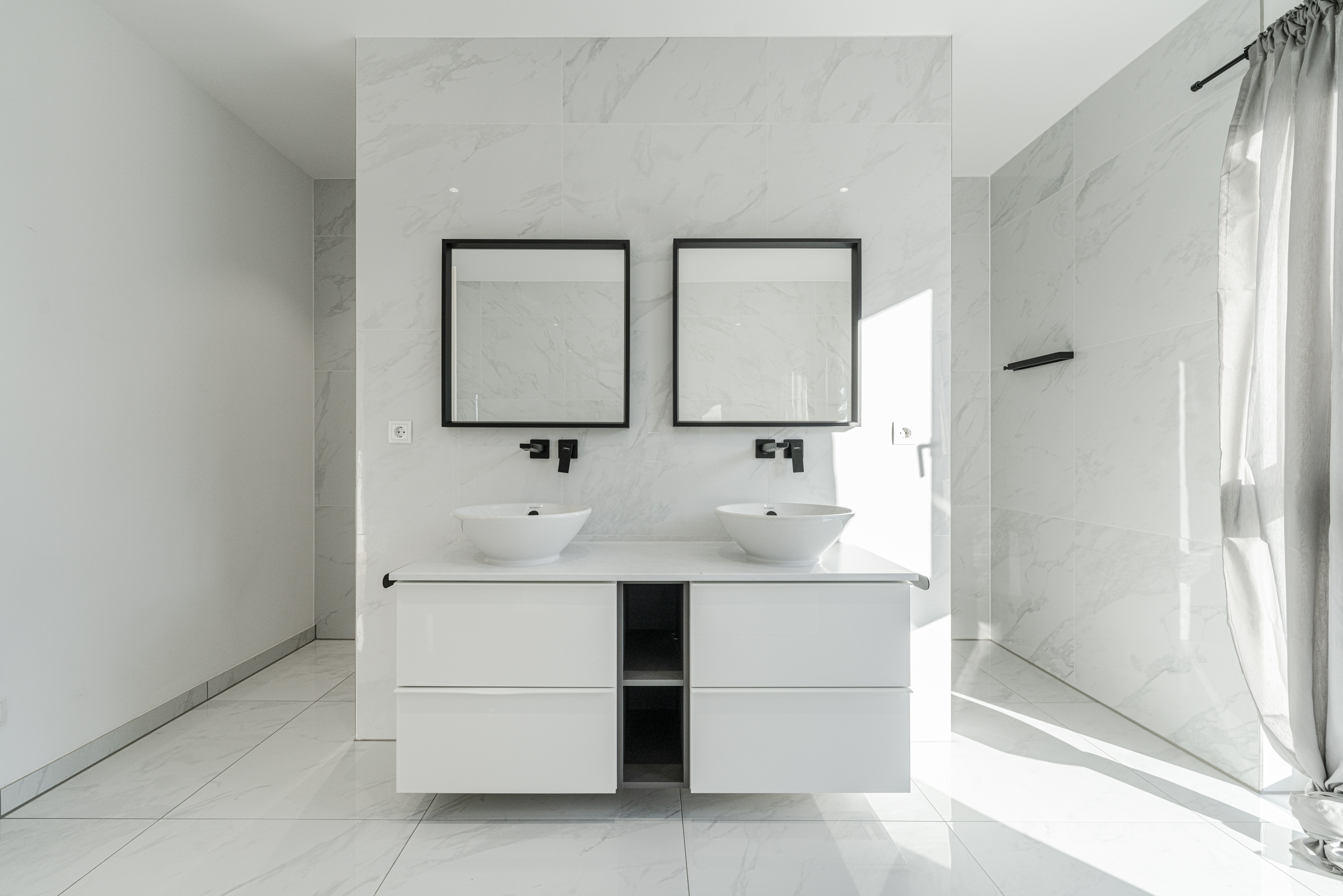 Modernes Badezimmer mit zwei Waschbecken, zwei Spiegeln und weißen Fliesen.