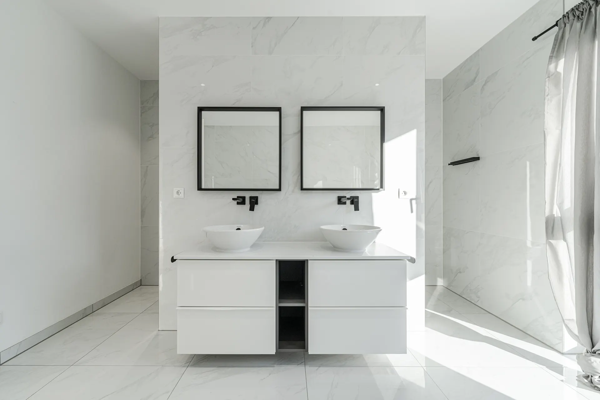 Modernes Badezimmer mit zwei Waschbecken, zwei Spiegeln und weißen Fliesen.