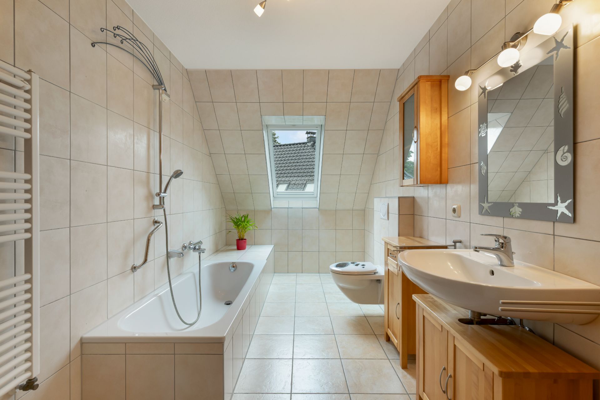 Helles Badezimmer mit Badewanne, Waschbecken, WC und Fenster, Fliesenboden und Holzschränken.