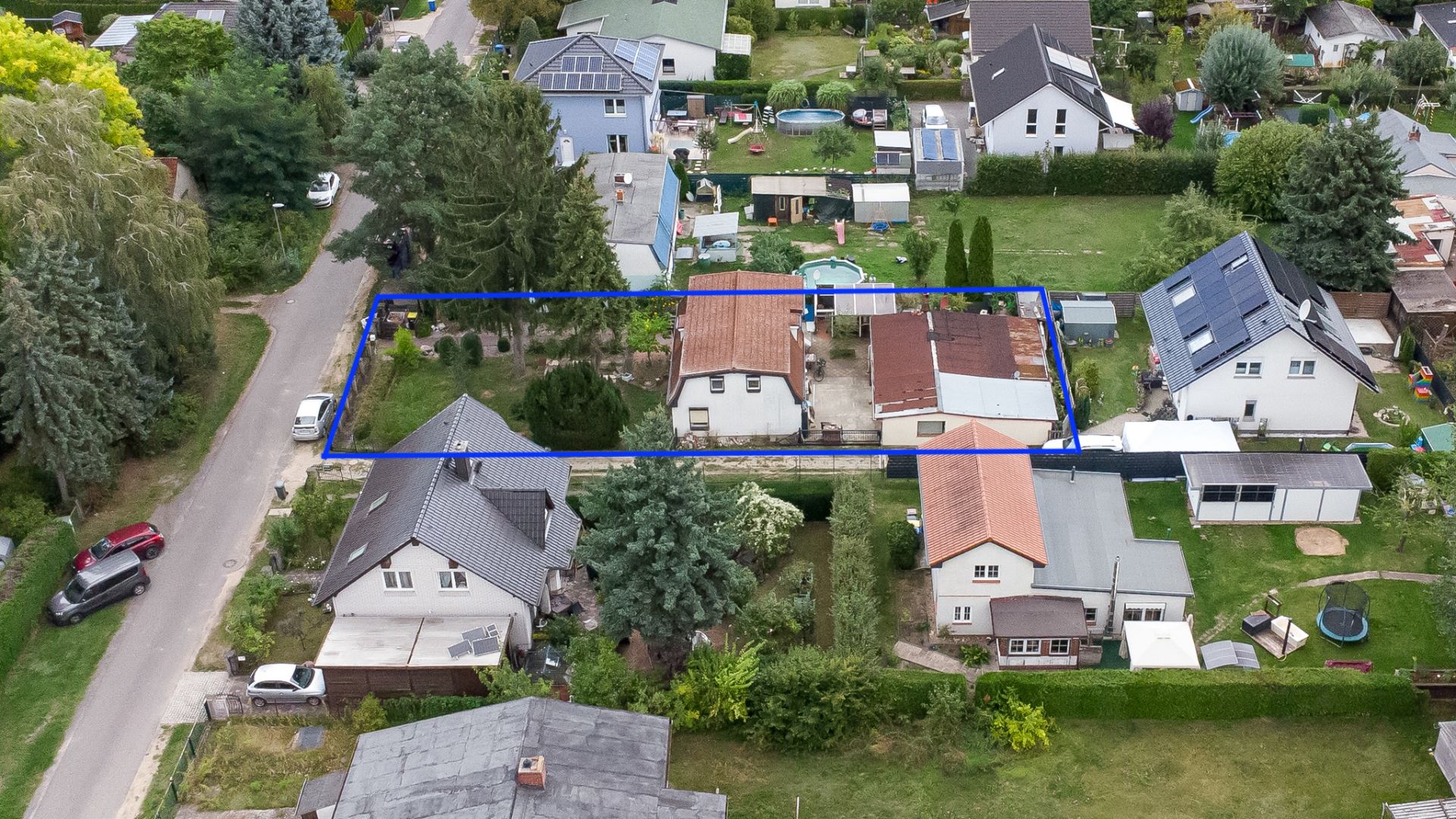 Luftaufnahme eines Grundstücks mit Haus und Nebengebäuden, blau umrandet, in Wohnsiedlung.