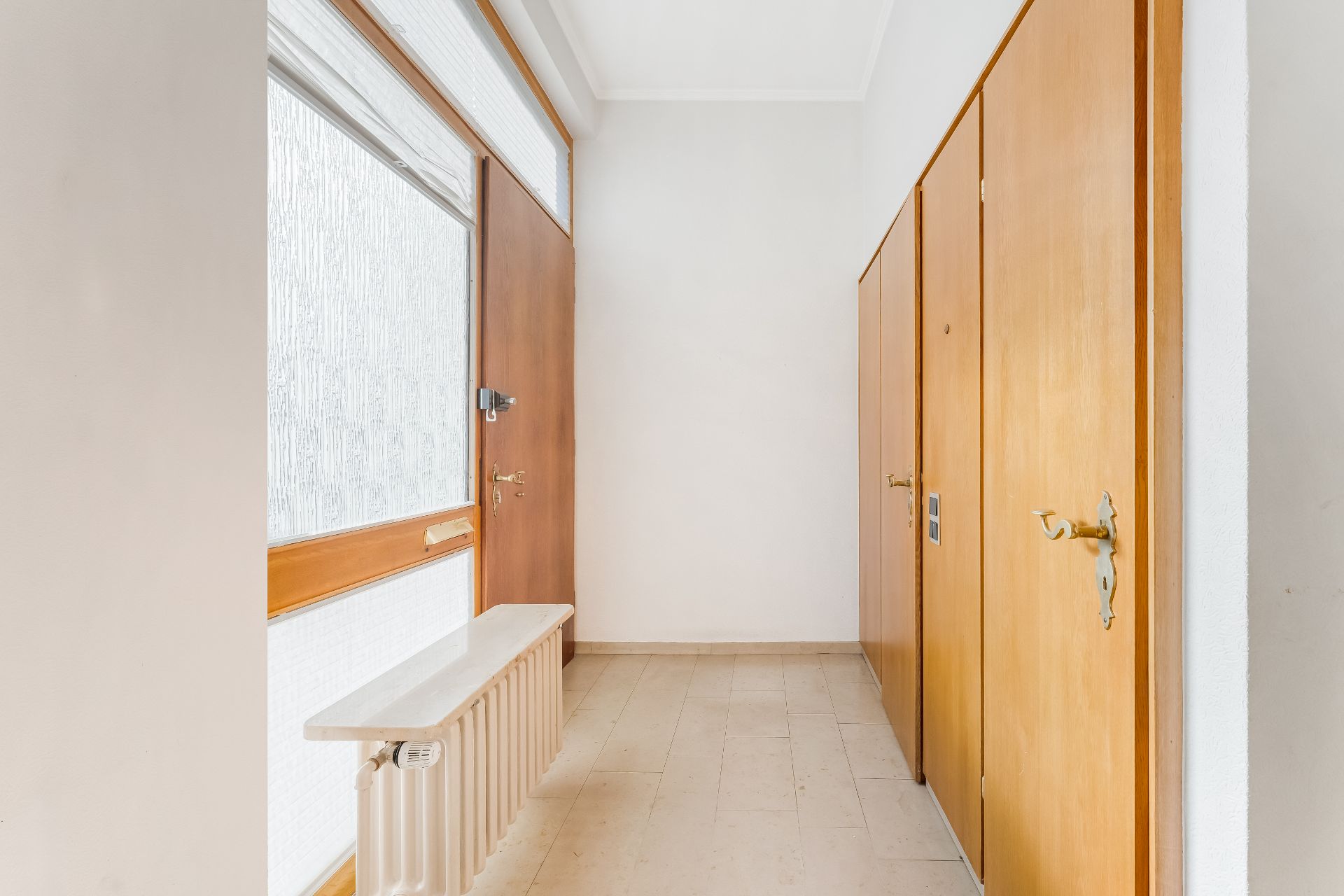Heller Flur mit Holztür, Garderobenschränken und Heizkörper unter Fenster.