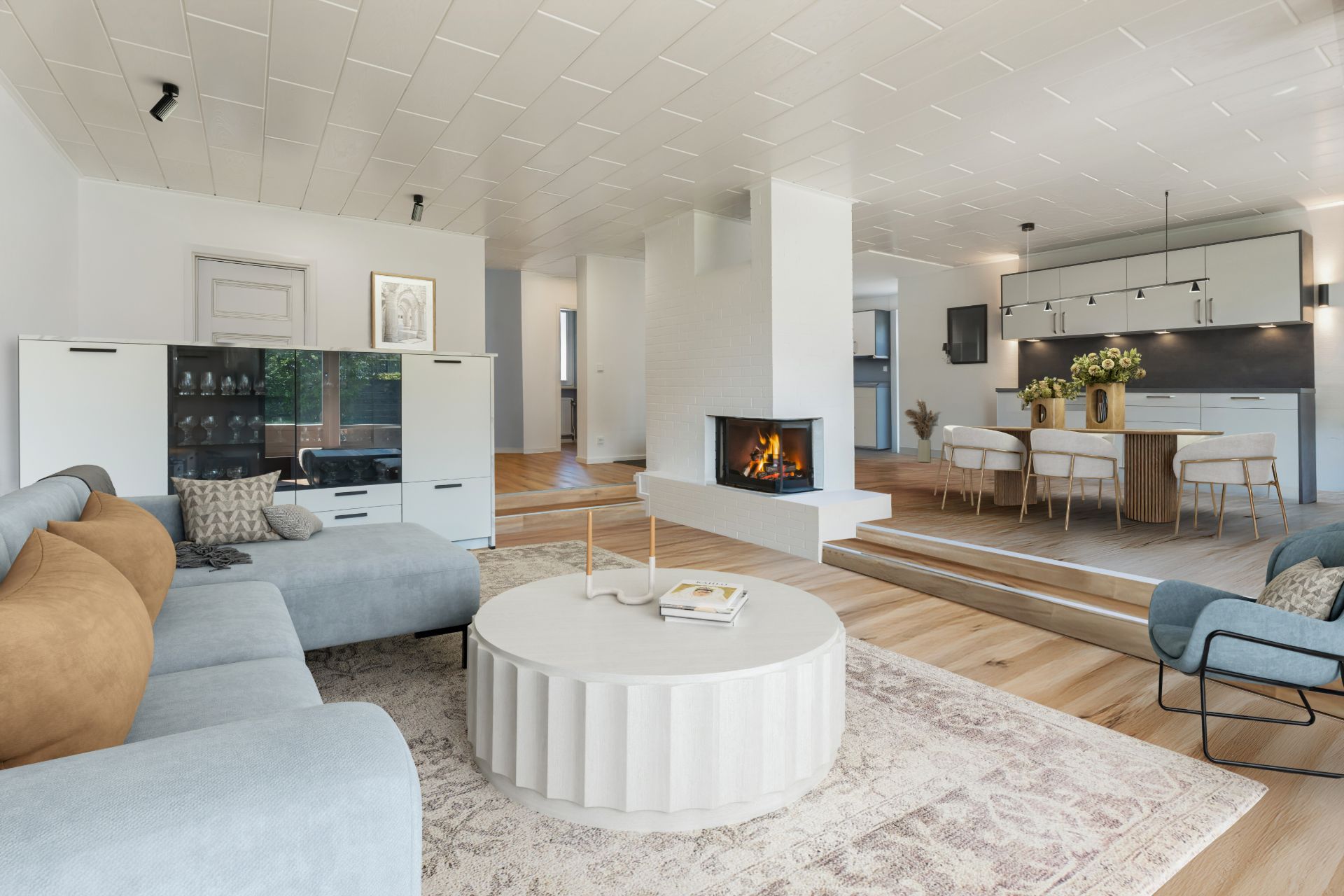 Helles Wohnzimmer mit Sofa, rundem Tisch, offenem Kamin und Blick zur Küche.