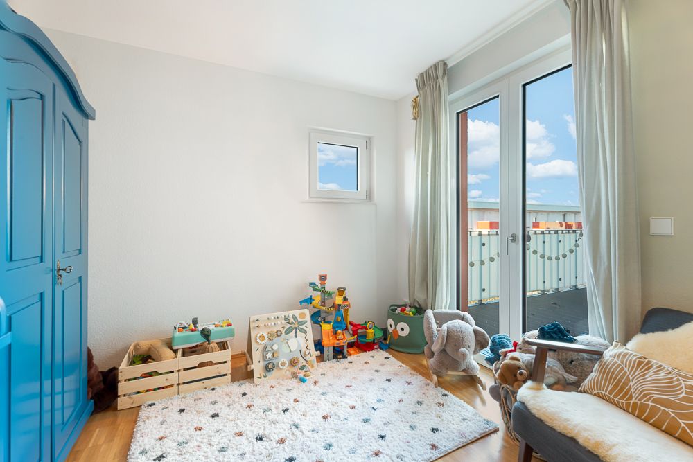 Helles Kinderzimmer mit Spielzeug, Teppich, blauem Schrank und Zugang zu einem Balkon.